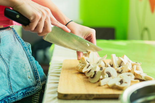 Female hands cut into large wooden mushrooms on a cutting board.