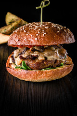 Cheese burger with grilled meat, cheese, tomato and potatoes on dark wooden surface. Ideal for advertisement. Close-up