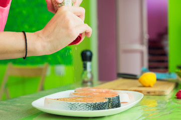 women's hands sprinkle from a handmade mills spices raw steak from salmon