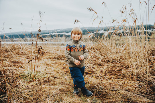 Outdoor portrait of a cute little boy of 4-5 years old, playing by the lake on a cold day