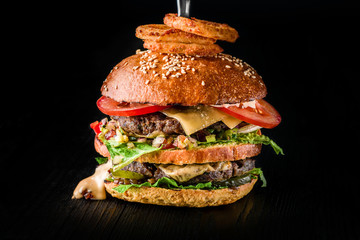 Cheese burger with grilled meat, cheese, tomato and with onion rings on dark wooden surface. Ideal for advertisement. Close-up