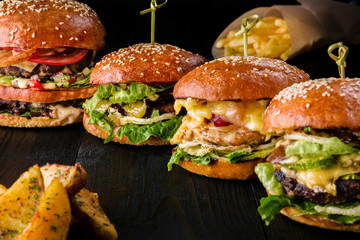 Four homemade hamburgers on wooden table. Buns with sesame seeds, beef burgers and various ingredients.
