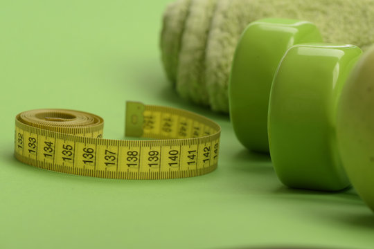 Tape measure in yellow color near lightweight barbells, close up