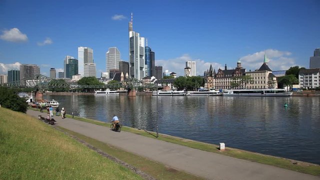 Skyline of the downtown in the city of Frankfurt Main. People jogging and riding bicycles at the riverwalk. 
