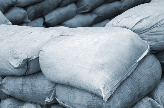 Background Of Many Dirty Sand Bags For Flood Defense. Protective Sandbag Barricade For Military Use. Handsome Tactical Bunker