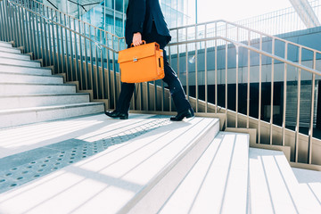 midsection contemporary business man walking upstairs in the city backlight, holding overnight bag...