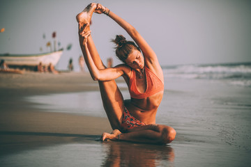 young flexible woman in swimsuit practicing yoga on beach at goa - obrazy, fototapety, plakaty