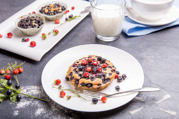 Berry muffins with blueberries and strawberries on a white plate on gray table served with milk and and fresh berries.