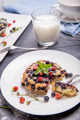 Berry muffins with blueberries and strawberries on a white plate on gray table served with milk and and fresh berries.