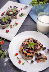 Berry muffins with blueberries and strawberries on a white plate on gray table served with milk and and fresh berries.
