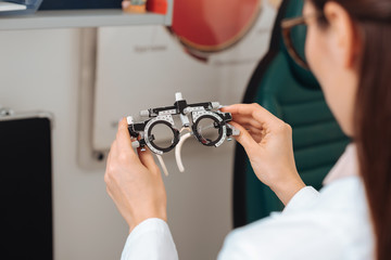 cropped shot of optometrist in white coat holding trial frame in hands