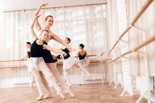 The trainer of the ballet school helps young ballerina perform different choreographic exercises.