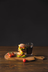 big sandwich with cherry tomatoes, cheese and glass of cola on wooden board
