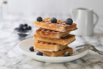 Waffles on a white plate decorated with blueberries with marbled background. copy space