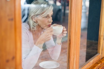 Thoughtful senior woman drinking coffee while sitting by table