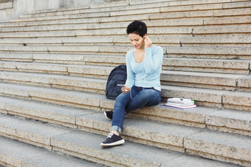 Young girl listening to music on university stairs