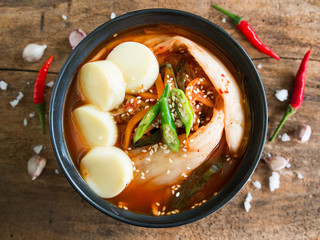 Kimchi soup with soft tofu and fresh chili on to, traditional Korean food on wooden table in top view.