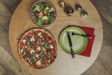 top view of arrangement of salad in bowl, italian pizza and dinnerware on wooden table