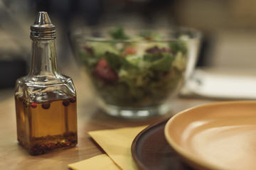 selective focus of oil in bottle, plates and salad in bowl on table