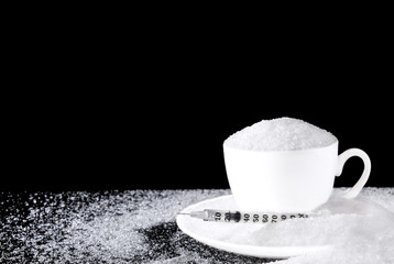 Pile white granulated sugar in white cup with syringe on dark background. With copy space for text.