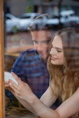 Happy couple holding smart phone while sitting at cafe