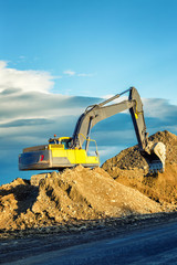 Excavator on a sand hill against a beautiful blue sky and mountains