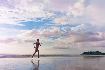 Fototapeta premium Healthy lifestyle concept. Jogging young woman on blue idyllic sunset thailand sea beach. Outdoors exercising