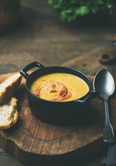 Corn creamy soup with shrimps served in individual pot with bread on board over rustic dinner table, copy space. Slow food, winter warming food concept