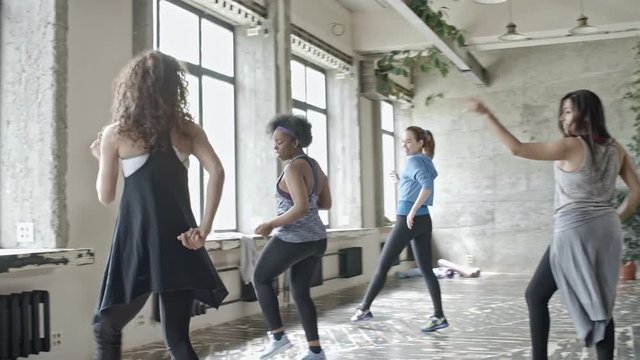PAN of female instructor with curly hair showing dance choreography to multiethnic group of young women during class in studio
