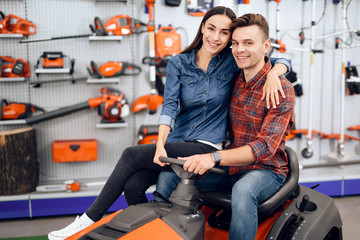 A young couple is sitting on a lawn mower.