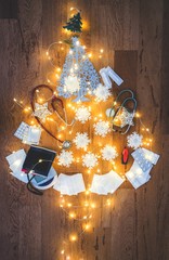 Top view of a Christmas tree composition with medical equipment: stethoscope, blood pressure measurement device, syringes, pills, Christmas lights and snowflakes decoration on wooden background
