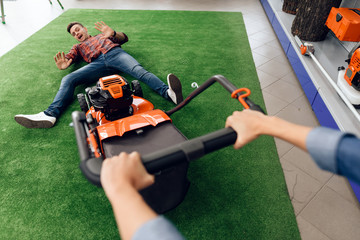 A guy is posing on the floor with a lawn mower in a tool store.