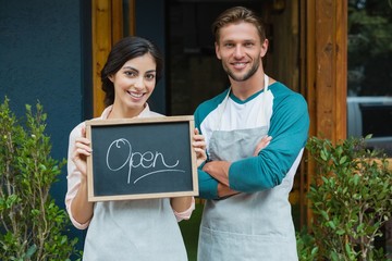 Portrait of smiling waiter and waitress standing with chalkboard