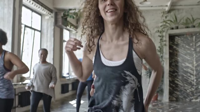 Tilt up of curly female dance teacher practicing choreography with group of young women