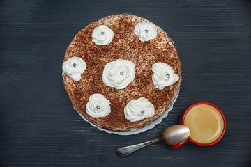 sour cream cake with cream and fresh coffee in a red mug on a dark wooden background