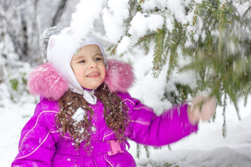 Little girl shaking the branch of pine tree covered by snow.