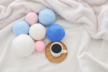 Cup of coffee and woolen balls over cozy and white blanket. Top view.