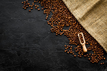 Coffee background. Roasted beans in scoop near canvas on black table top view copyspace