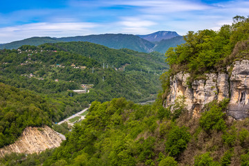 A huge rock with a green forest towers over the canyon with a road going uphill. Mountain valley on the way to Krasnaya Polyana from Adler, Sochi, Russia.