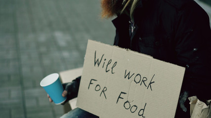 Homeless young man beg for money shaking cup to pay attention people walking near beggar at the...