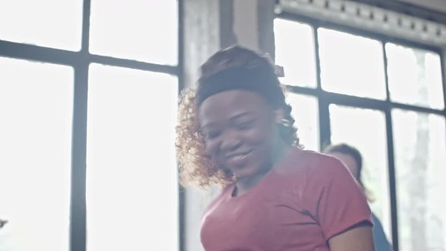 PAN of energetic African woman with curly hair dancing zumba in group class