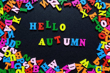 concept design - the word HELLO AUTUMN from multi-colored wooden letters on a black background, creative idea