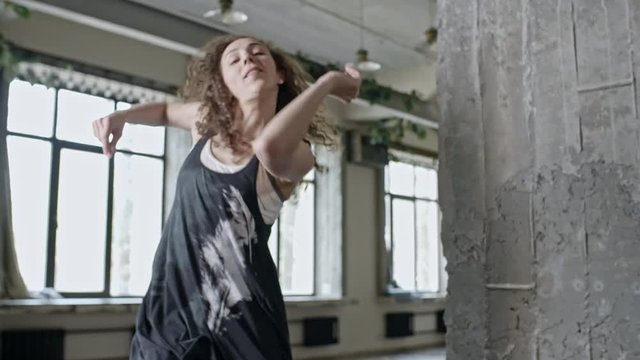 PAN with slowmo of curly young woman dancing in empty studio and looking at camera