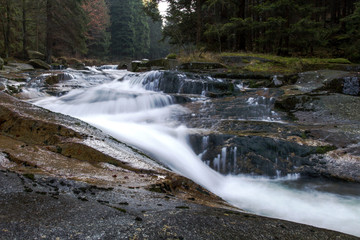Naklejka premium Fast-flowing water, picturesque blurred shapes of the water movement. Rocky shores. Beautiful Stream in the forest. 
