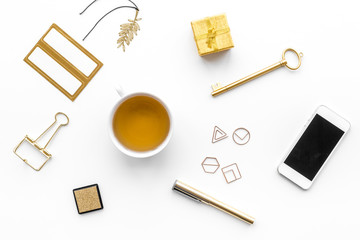 Office desk in trendy gold color. Glittering stationery near cup of tea, cell phone   on white background top view