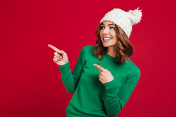 Smiling brunette woman in sweater and funny hat pointing away