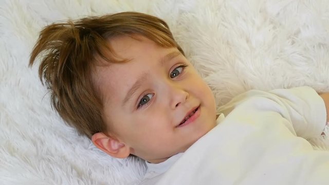 Close-up of a child holding on a white blanket looking at the camera at a slowed pace. The child shows joy and a big smile