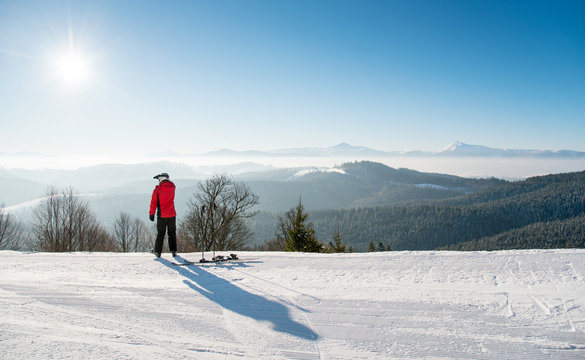 Rearview shot of a skier resting after the ride standing on top of the ski slope looking around enjoying beautiful view of snowy mountains on a sunny winter day seasonal recreational extreme active