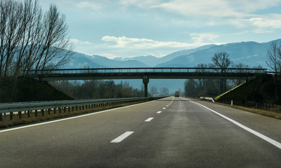 Two line wide highway on a cloudy winter day leading to the mountains through rural landscape