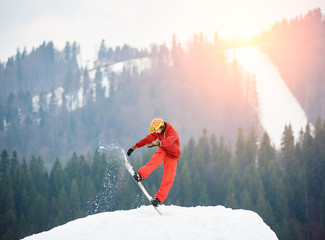 Man snowboarder jumping on the top of the snowy hill with snowboard in the evening at sunset. Ski...